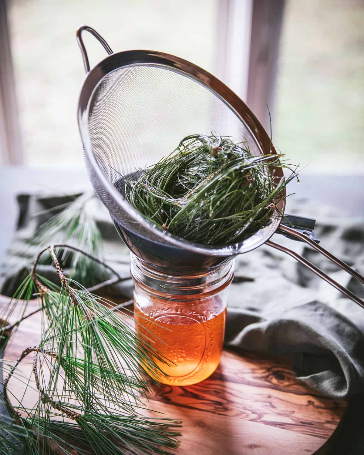 A mesh strainer filled with pine needles atop a jar of strained honey.