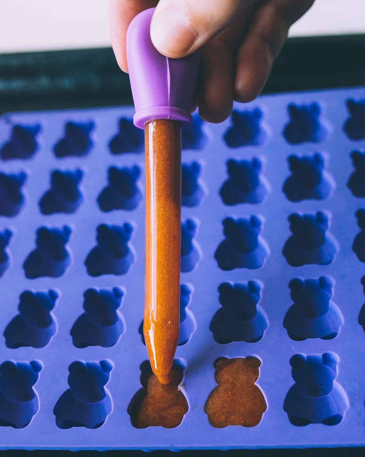 Gummy bear molds with a dropper pouring the liquid into each mold.