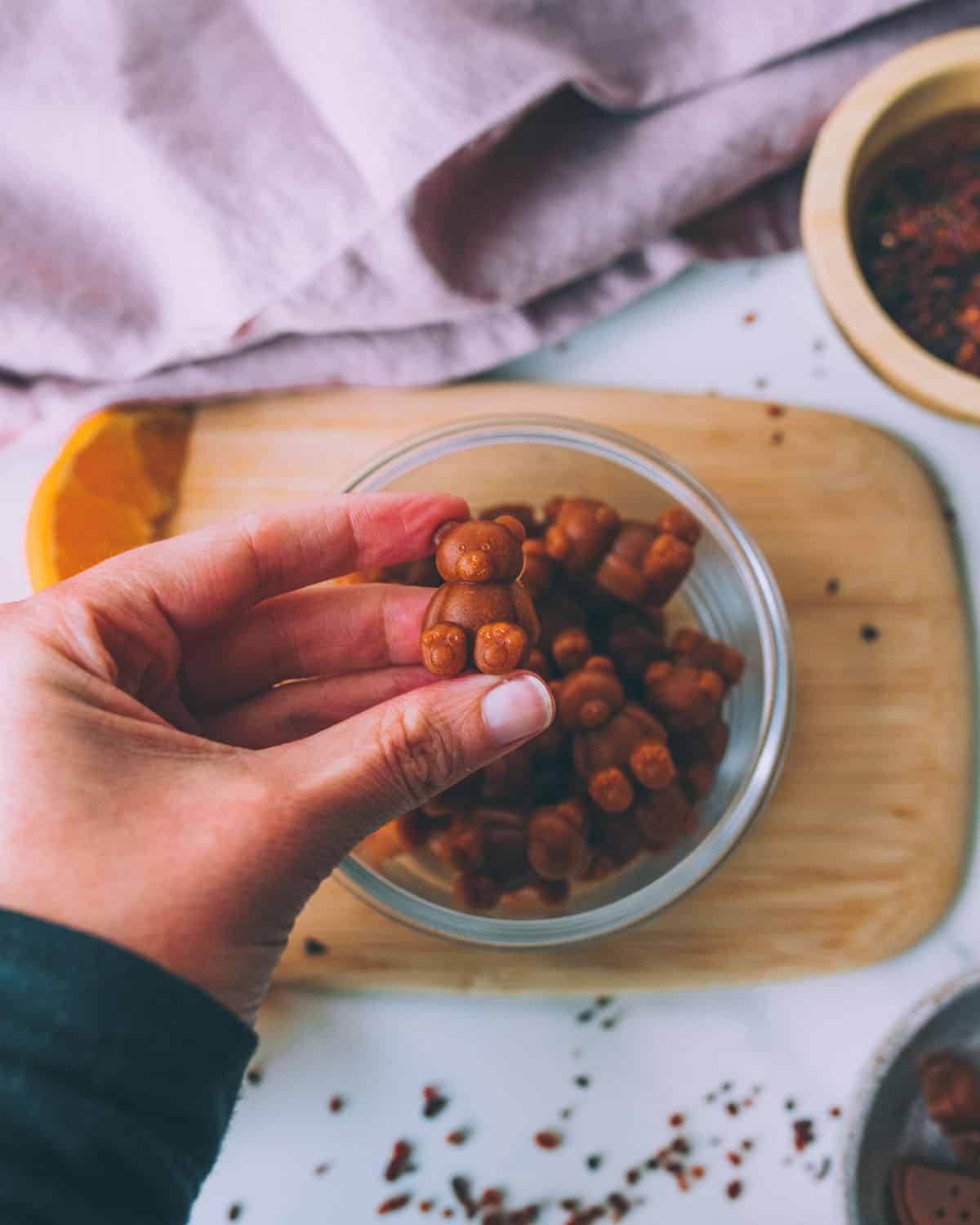 Bear shaped vitamin C gummies in a bowl, with a hand holding one up to see closely. 