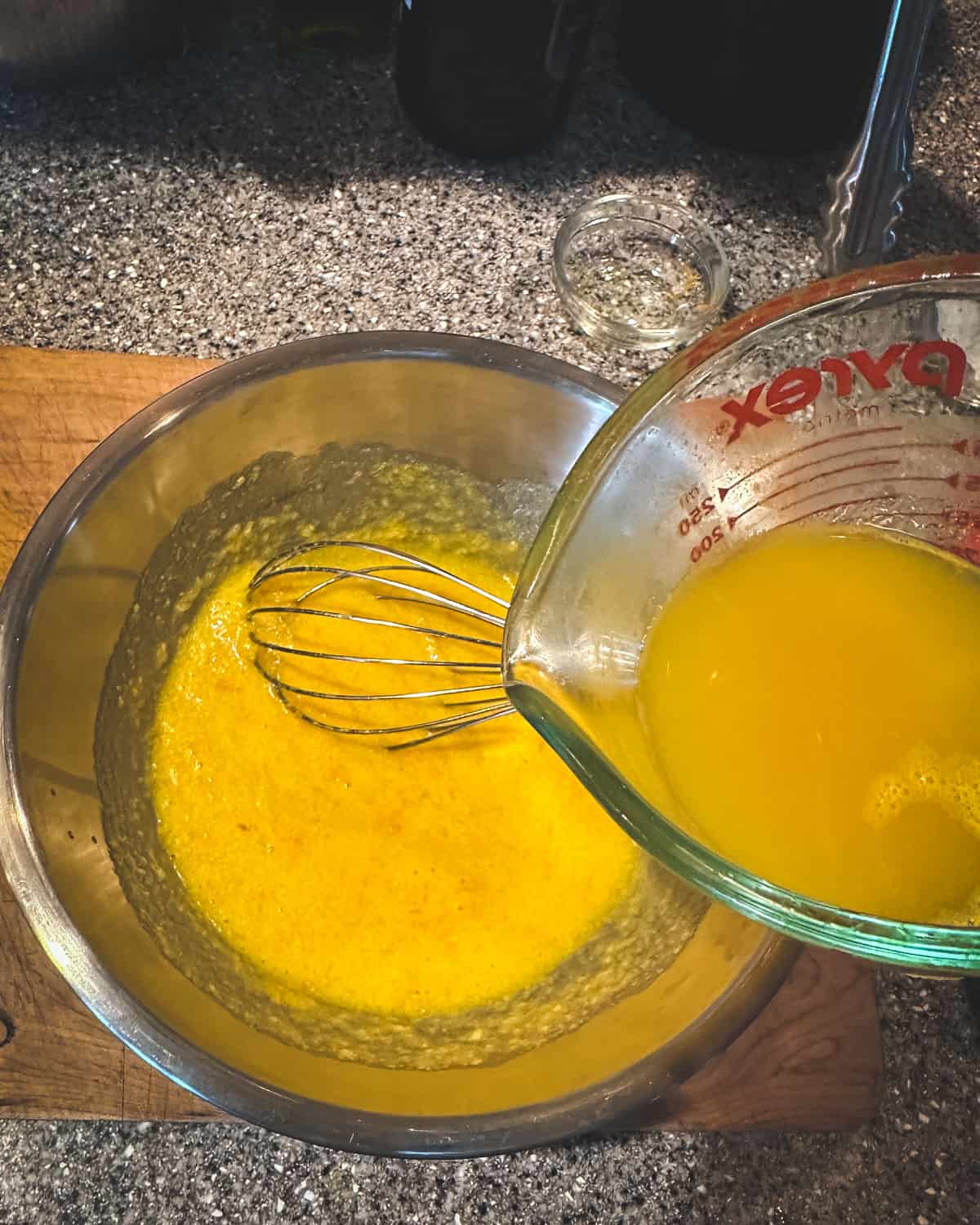 Orange juice pouring into the metal bowl with the other curd ingredients. 