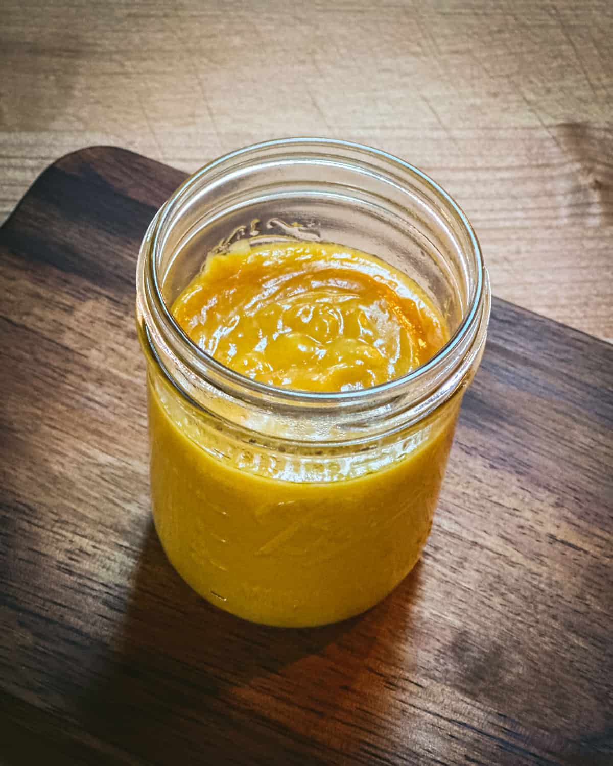 A jar of finished orange curd, on a wooden cutting board. 