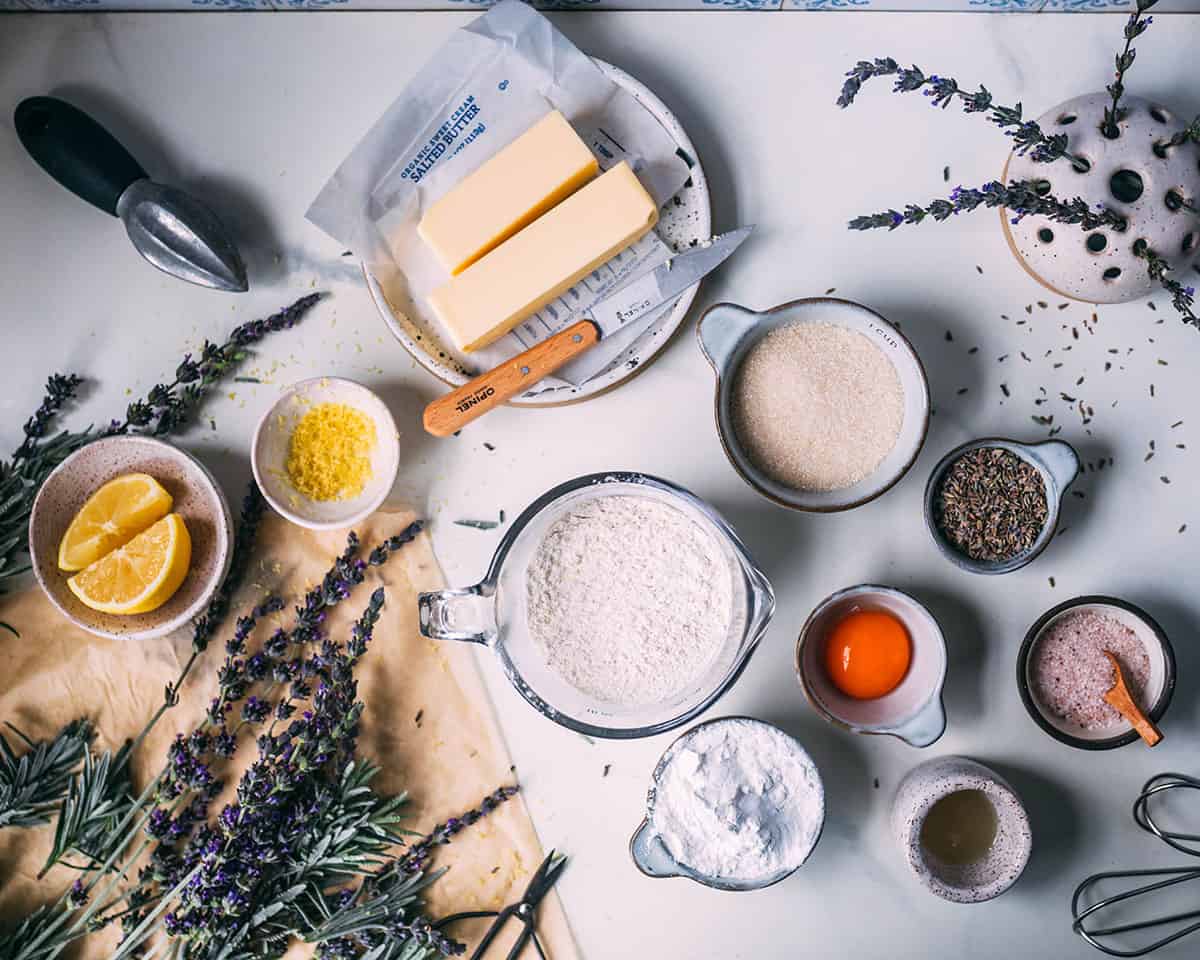 Ingredients in small bowls for lavender shortbread cookies, surrounded by fresh lavender.