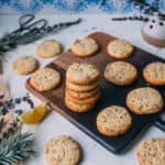 A stack of lemon lavender shortbread cookies on a dark wooden cutting board with a light background, surrounded by other lemon lavender shortbread cookies, and fresh lavender.