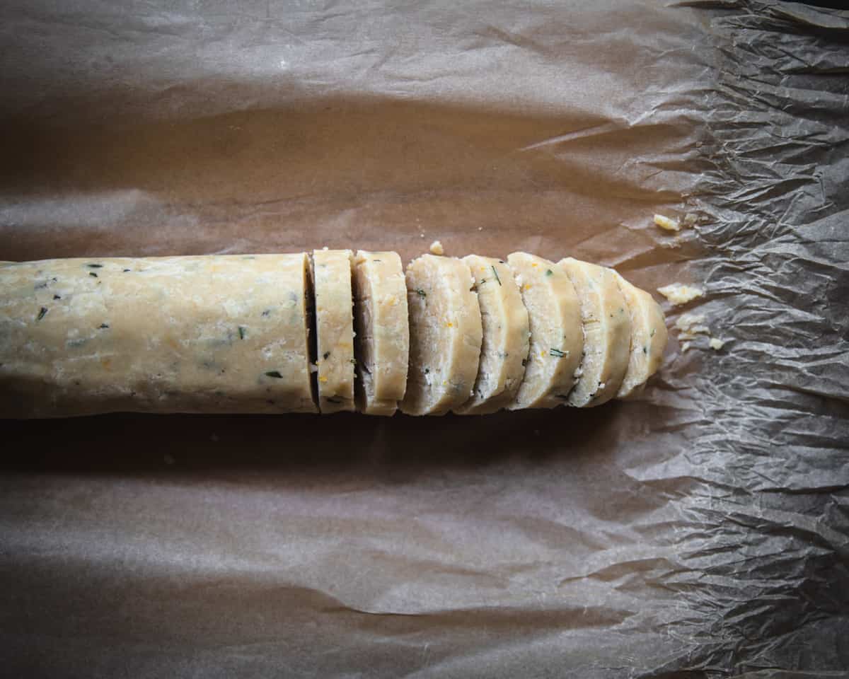 Parchment paper unwrapped showing the log of dough, half of it sliced into cookies. 