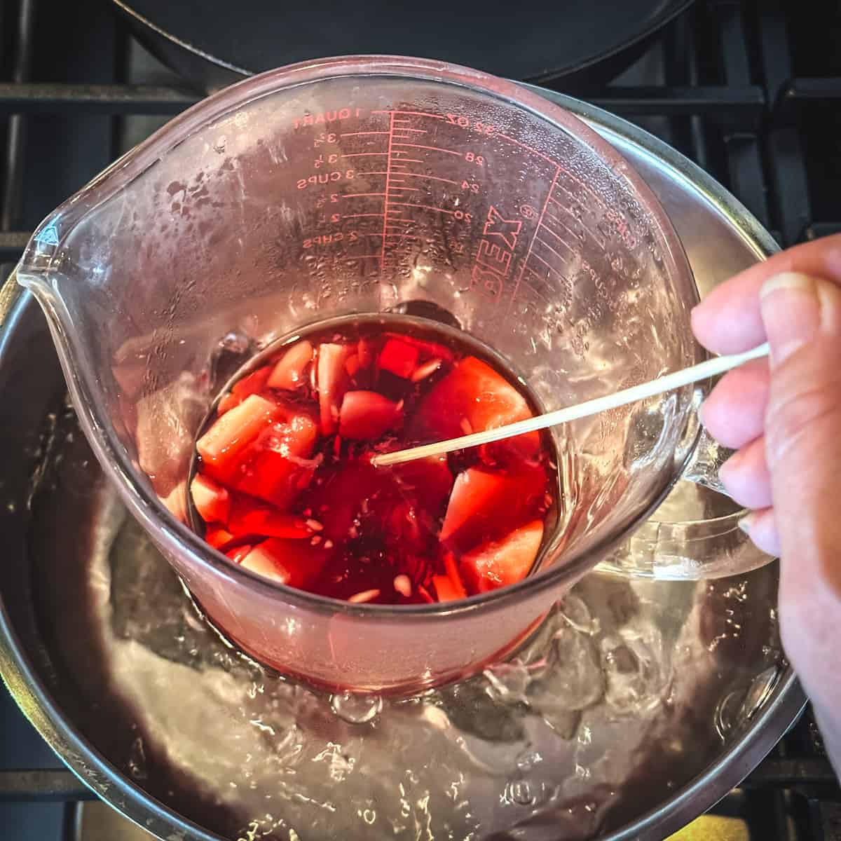 A makeshift double boiler with red infused oil and melting beeswax and cocoa butter. 