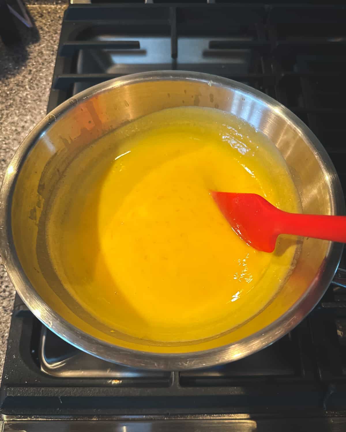 Orange curd thickening in the double boiler, stirred with a red spatula. Top view.