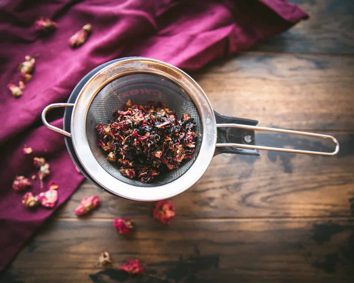 A mesh sieve sitting atop a jar straining the rose petals out of the infused oil. 