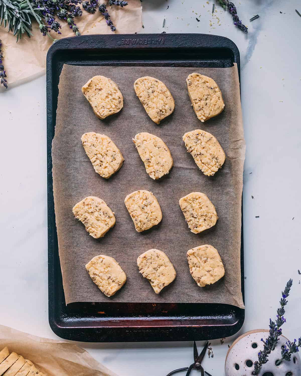 Chilled dough rounds flat on a baking sheet lined with parchment paper, surrounded by fresh lavender.