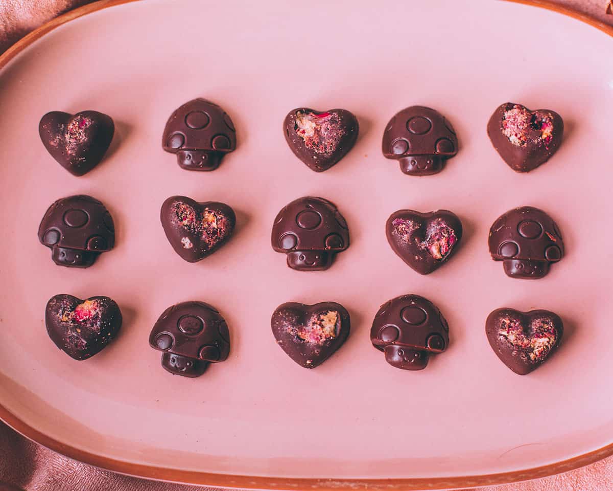 Mushroom chocolates lined up in heart and mushroom shapes on a pink oval plate.