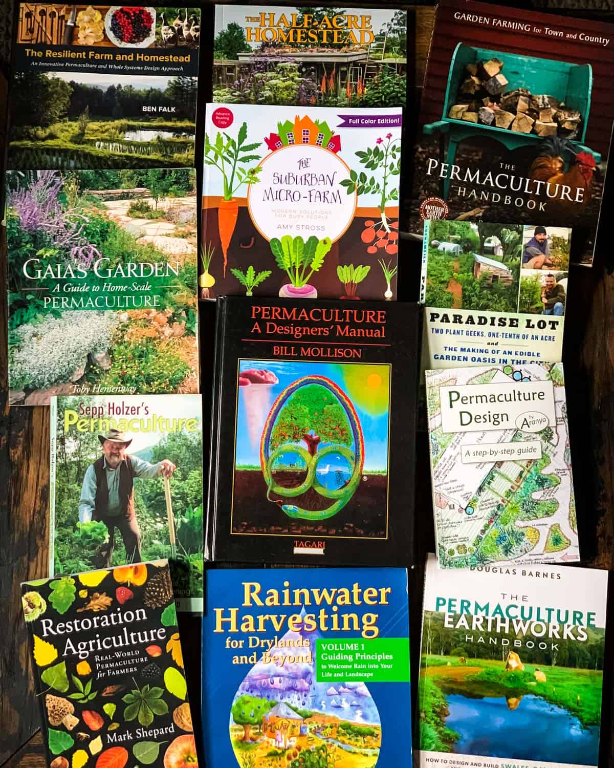 A photo of permaculture books laying face up on a wooden table so the covers can be seen.