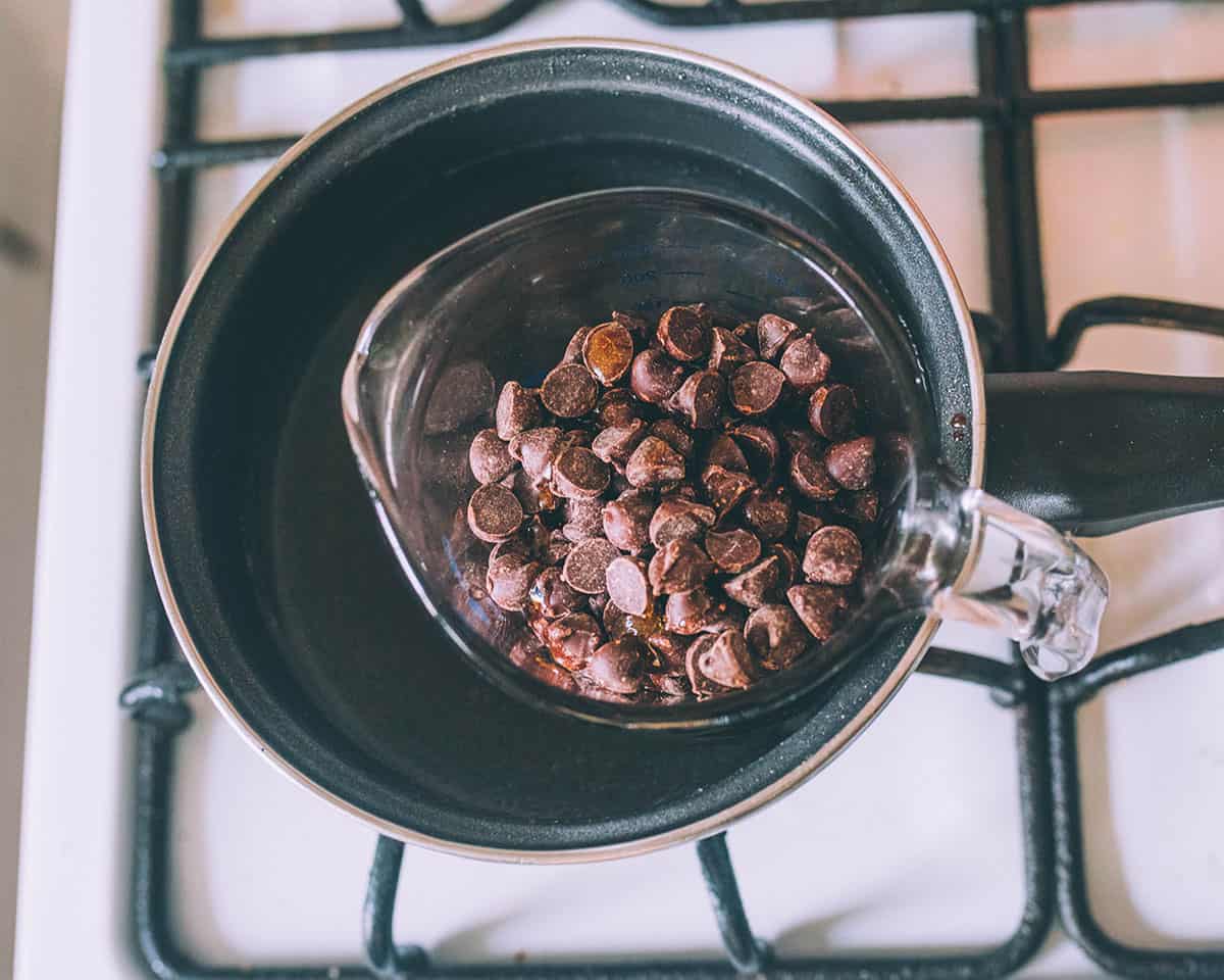 A makeshift double boiler with a pot and a pyrex measuring cup that has dark chocolate chips in it.