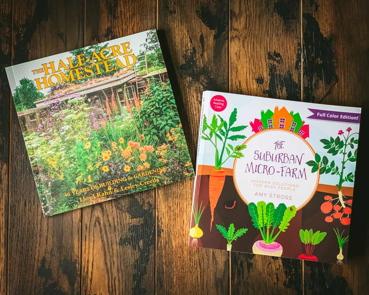 Two permaculture books face up on a dark wood surface.