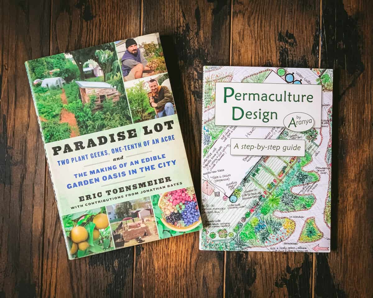 Two permaculture books face up on a dark wood surface. 