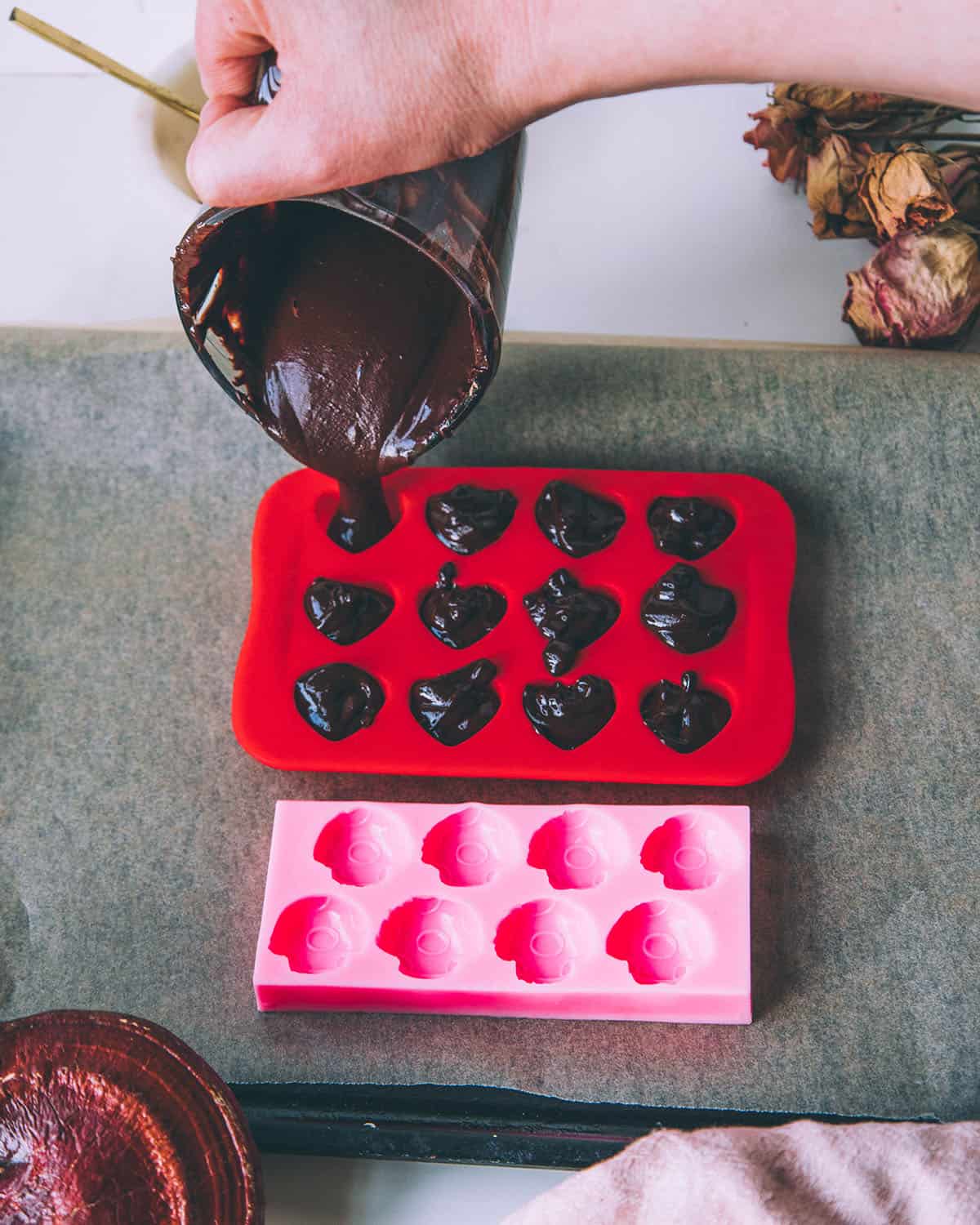 Melted chocolate mixture pouring into the silicone molds, some with hearts, some with mushroom shapes.