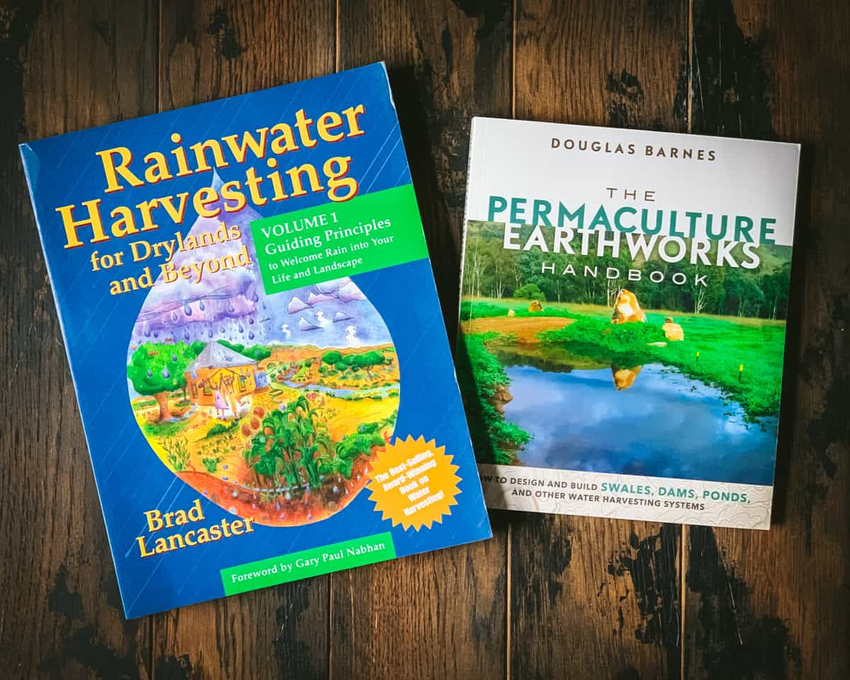 Two permaculture books face up on a dark wood surface. 