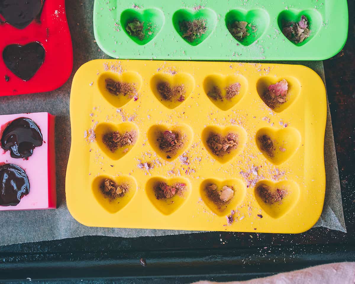 Silicone molds that are heart shaped with pink rose petals sprinkled in the bottoms of the mold shapes.