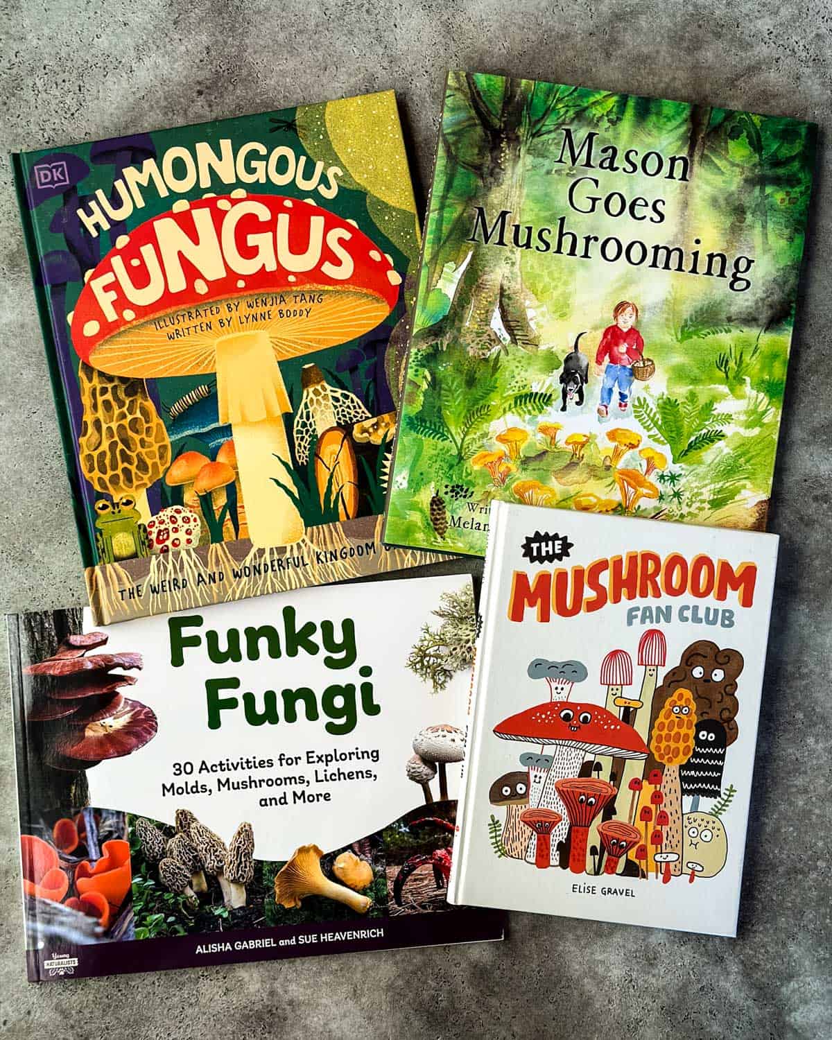 4 mushroom foraging books for kids face up on a gray surface.