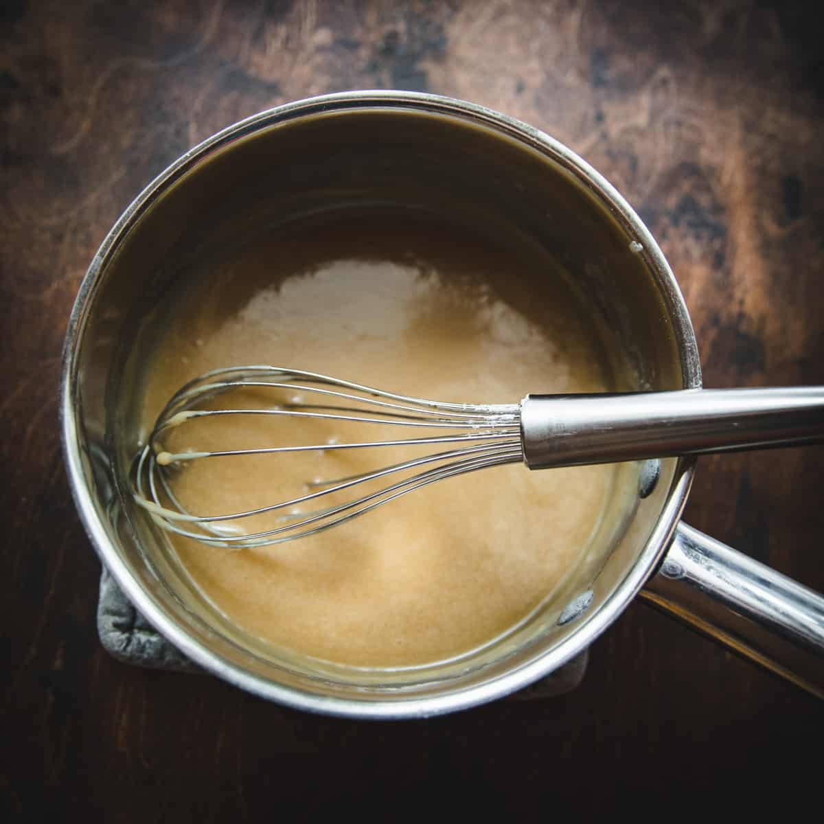 Maple icing ingredients in a pot with a whisk in it. 