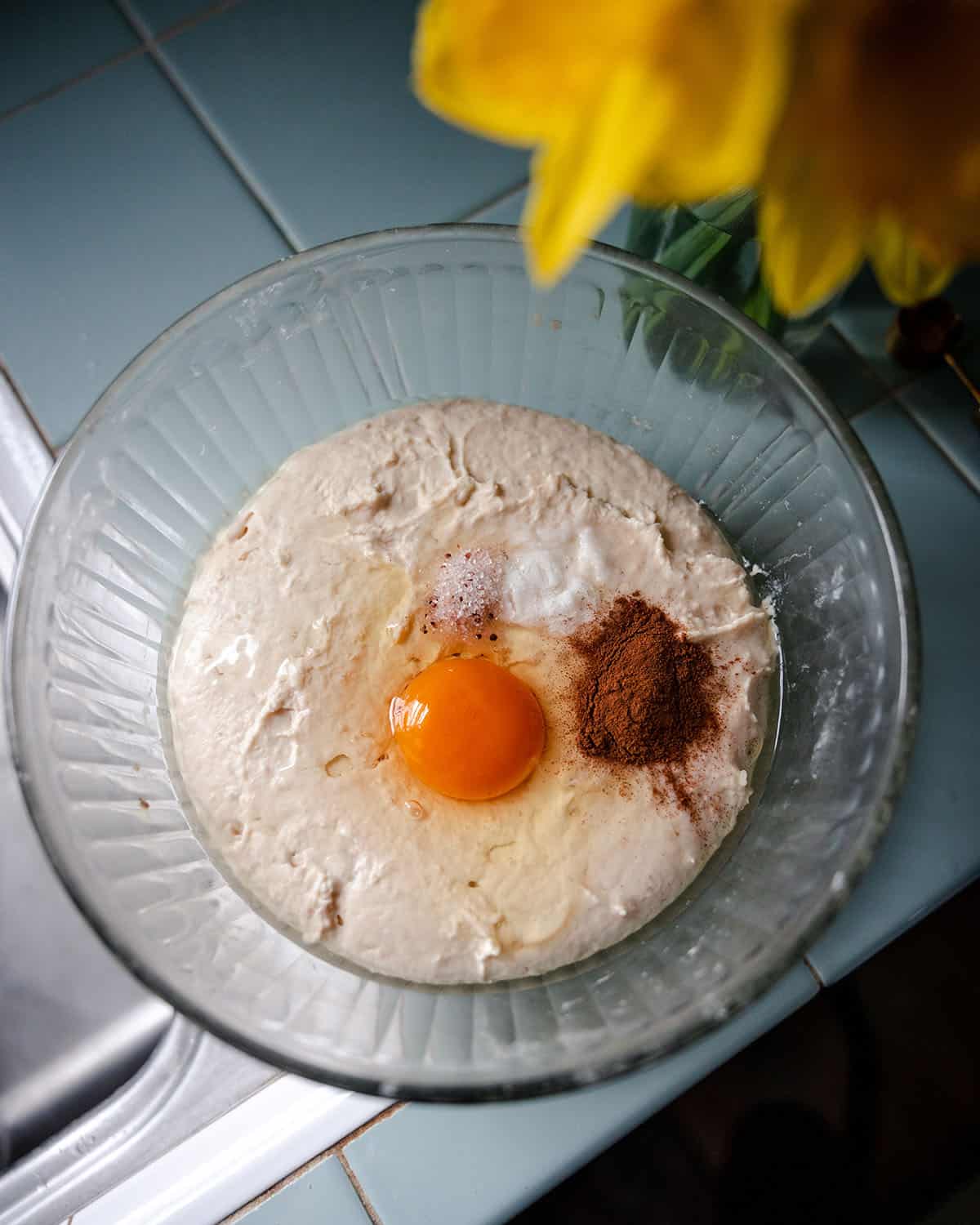 A mixing bowl with the sourdough mixture with an egg, cinnamon, salt, and baking powder ready to stir in. 