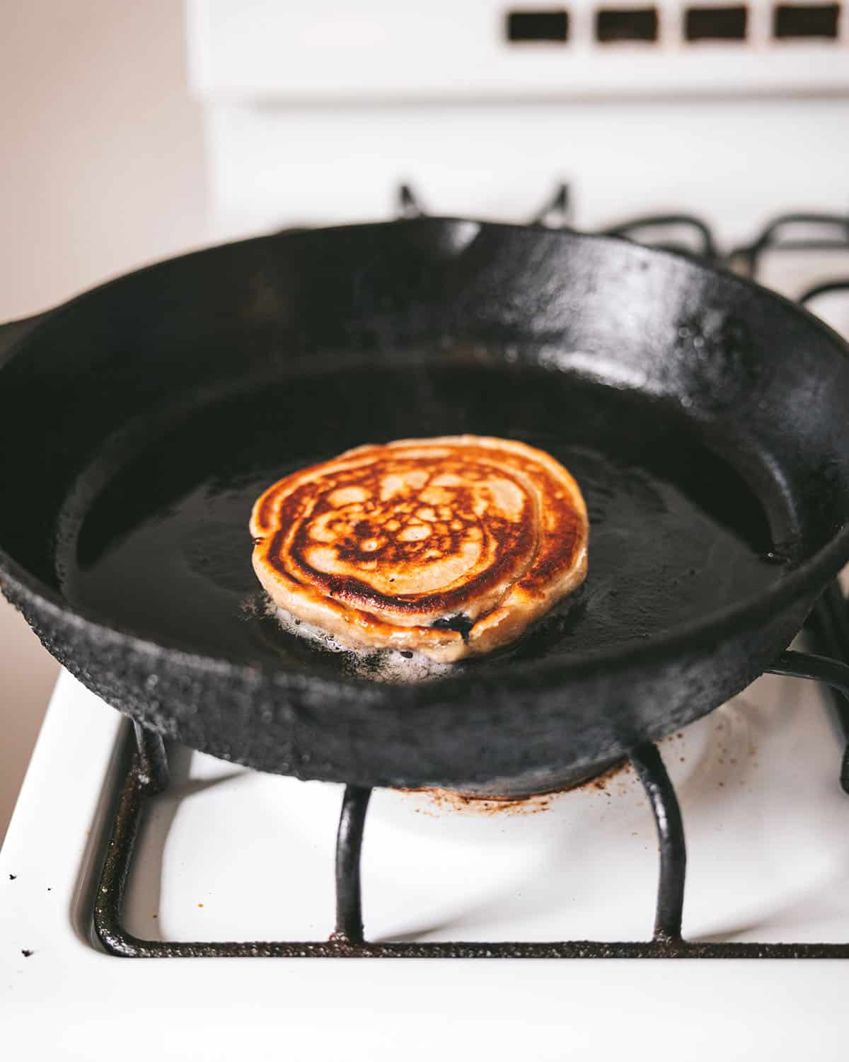 A flipped pancake cooking on the second side in a cast iron skillet.