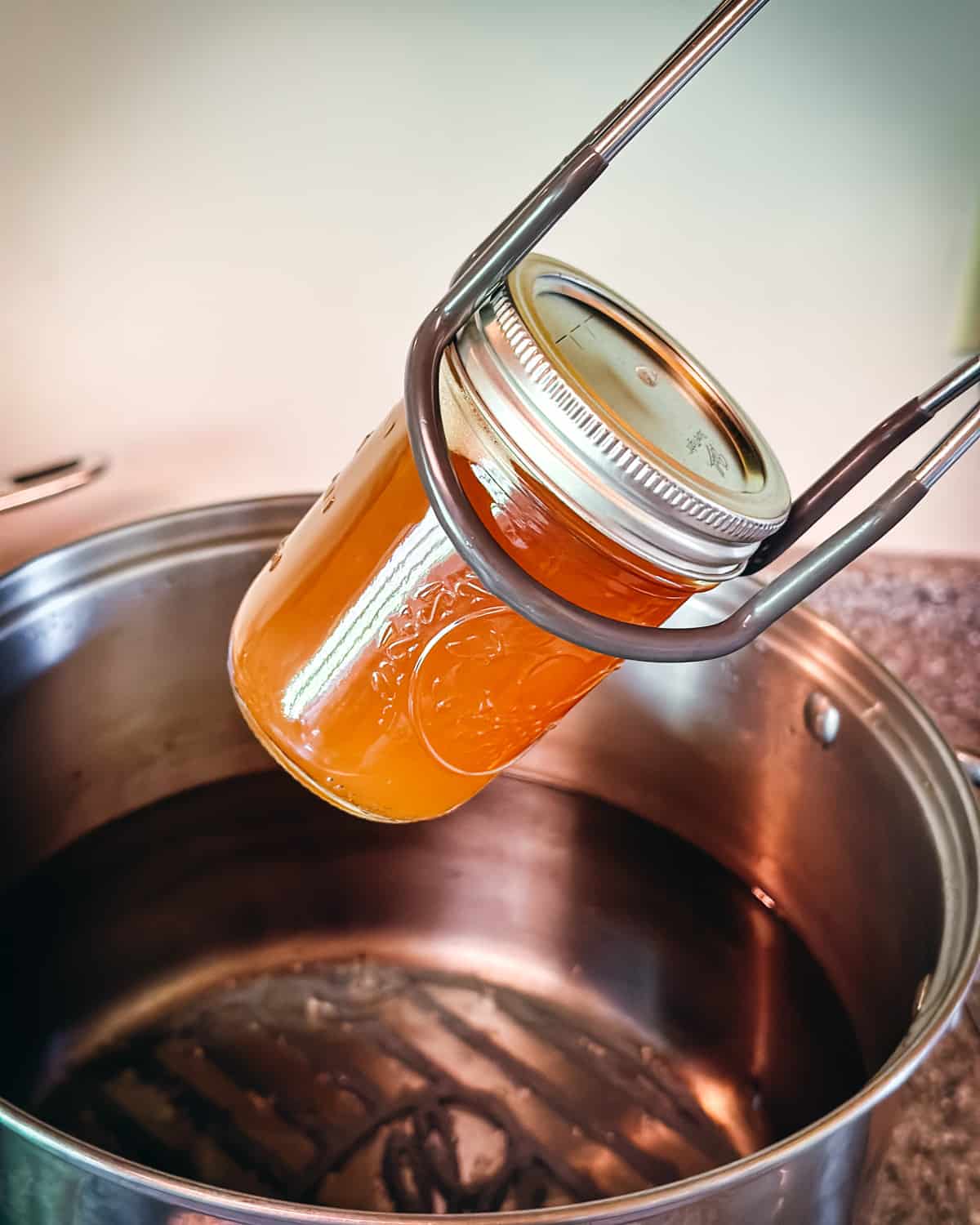 A jar lifter pulling a jar of dandelion jelly out of a pot of boiling water to process for canning.
