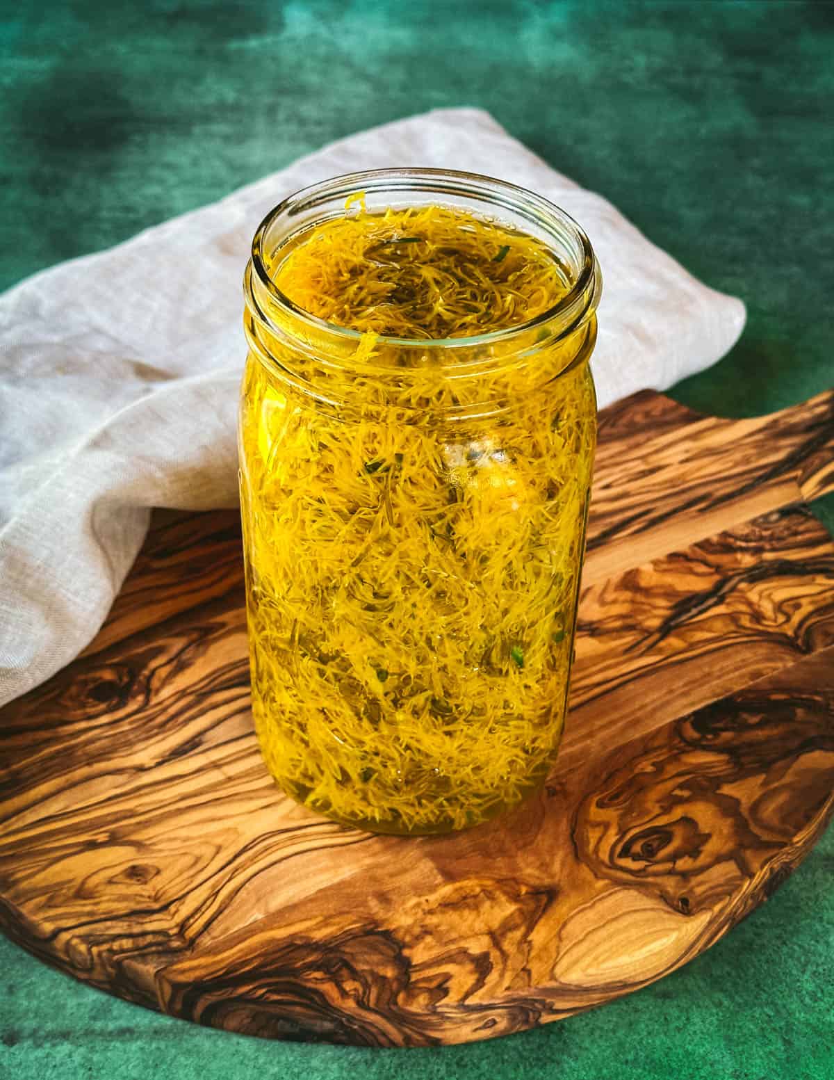 A jar of dandelion petal steeping, on a wooden cutting board with a green background.