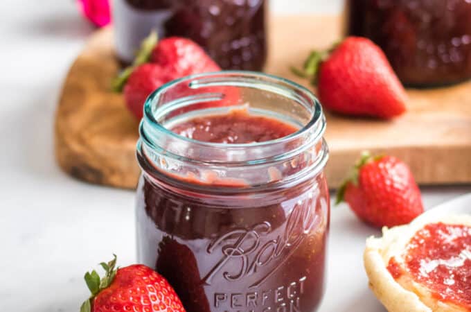 A jar of strawberry honey butter surrounded by fresh whole strawberries.