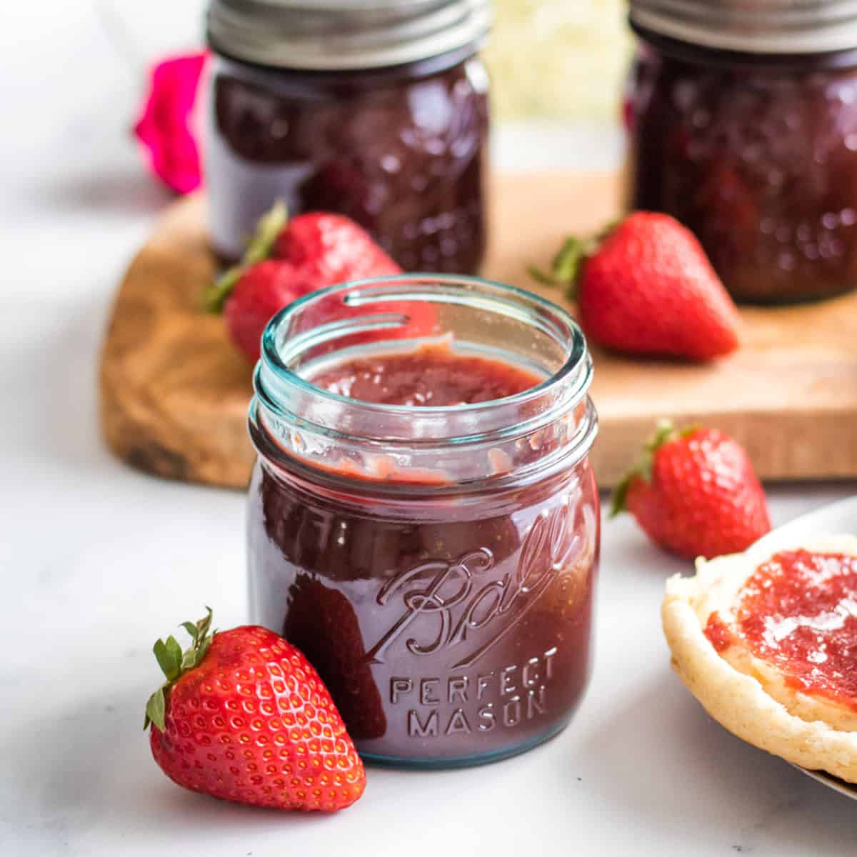 A jar of strawberry honey butter surrounded by fresh whole strawberries. 