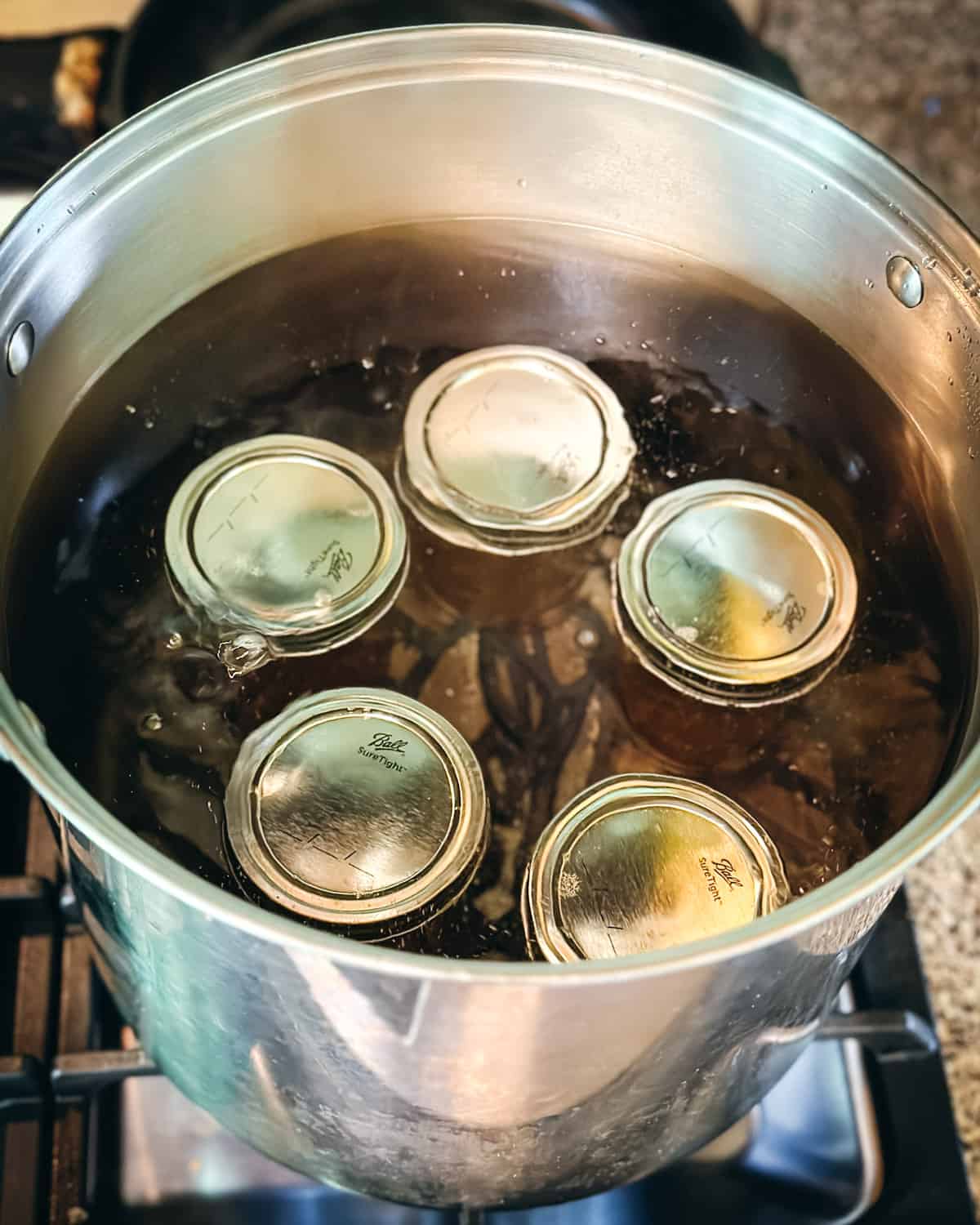 Jars of dandelion jelly in a boiling pot of water processing for canning.