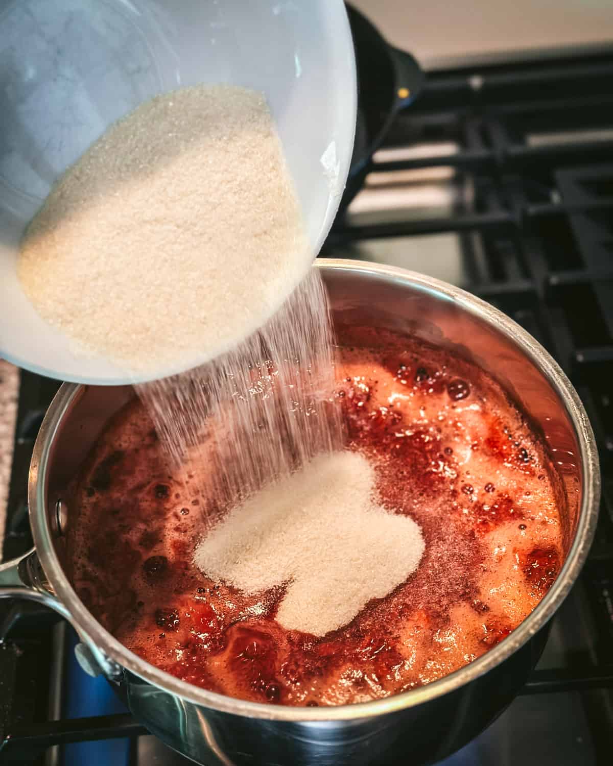 Sugar and pectin mixture pouring into the boiling strawberries saucepan. 