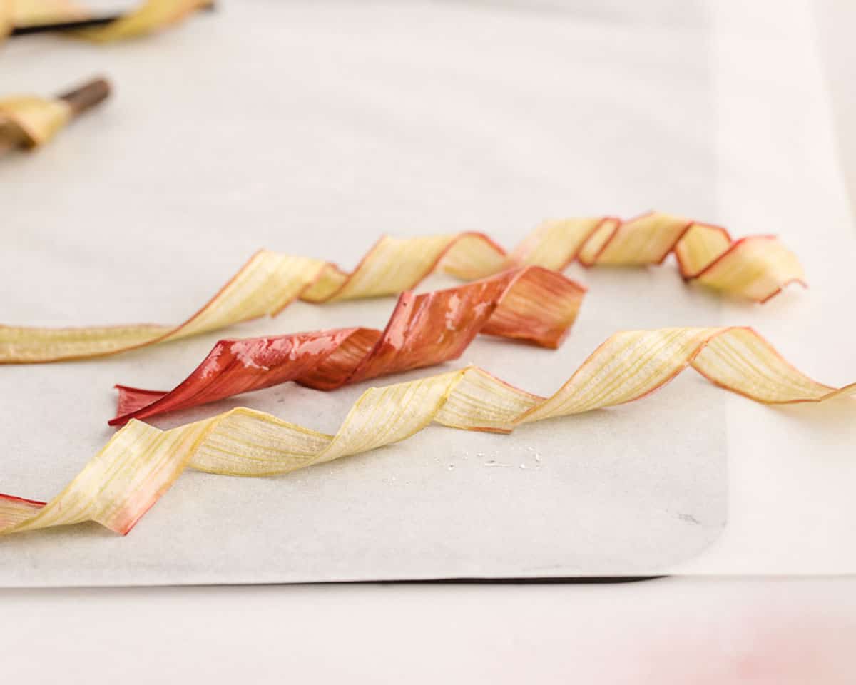 Candied rhubarb ribbons on a parchment lined baking sheet. 