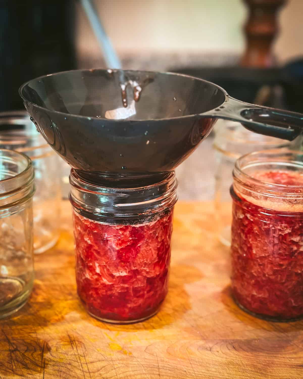 A funnel over jam jars with strawberry jam pouring in. 
