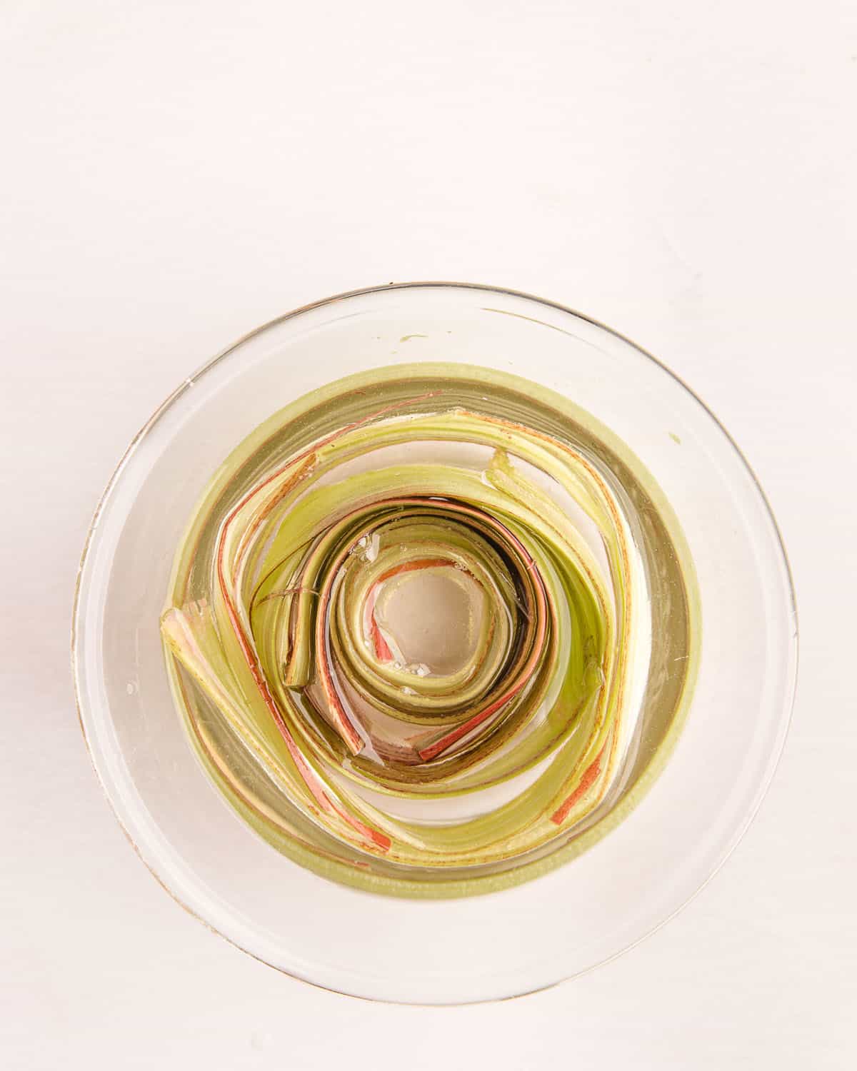 Top view of a clear bowl with thin rhubarb strips soaking in simple syrup.