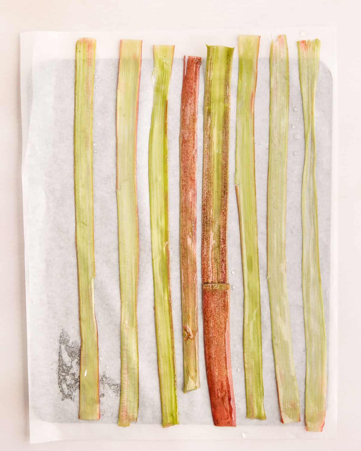 Rhubarb strips laying flat on a parchment paper lined baking sheet. 