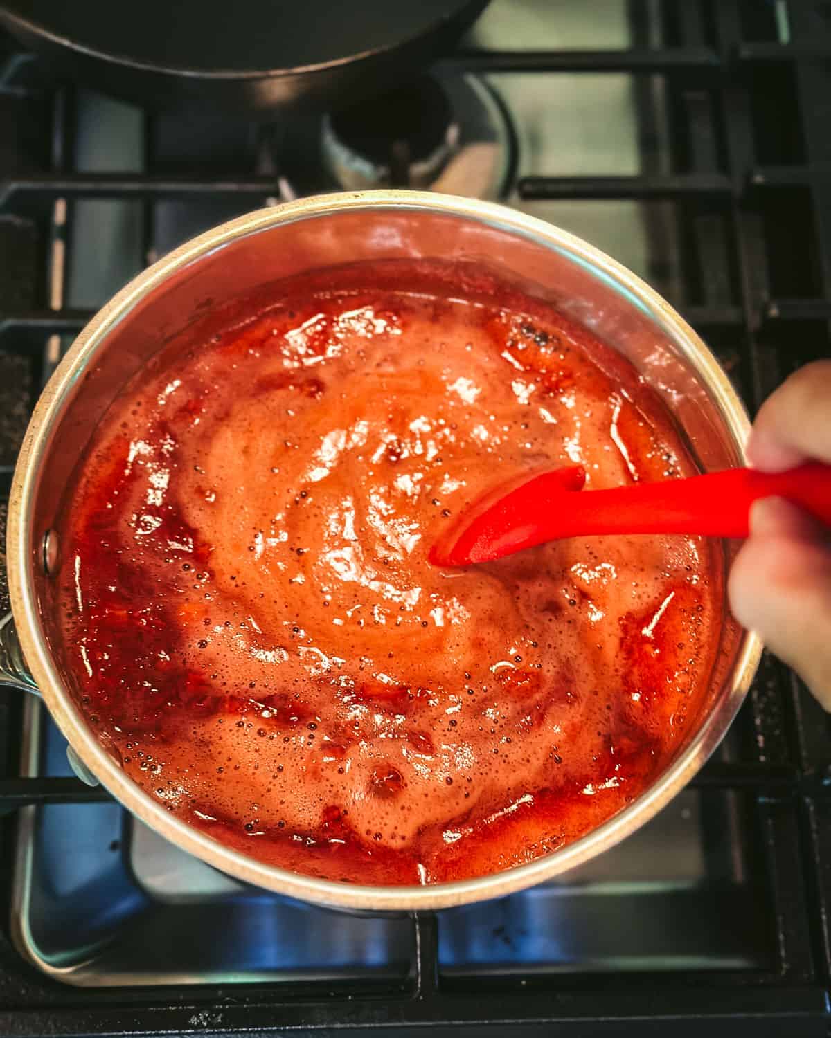 A pot of strawberry jam being stirred and cooking on the stove. 