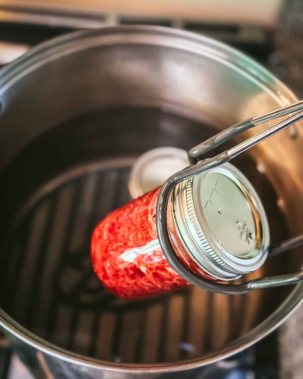 A jar lifter placing filled strawberry jam jars into a hot water bath for canning. 