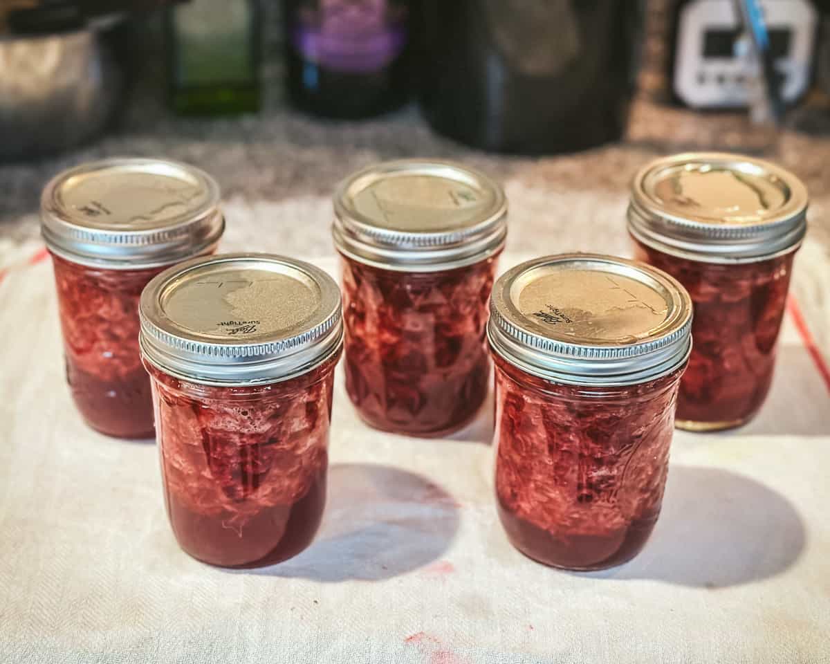 Canned jars of strawberry jam cooling out on the countertop.