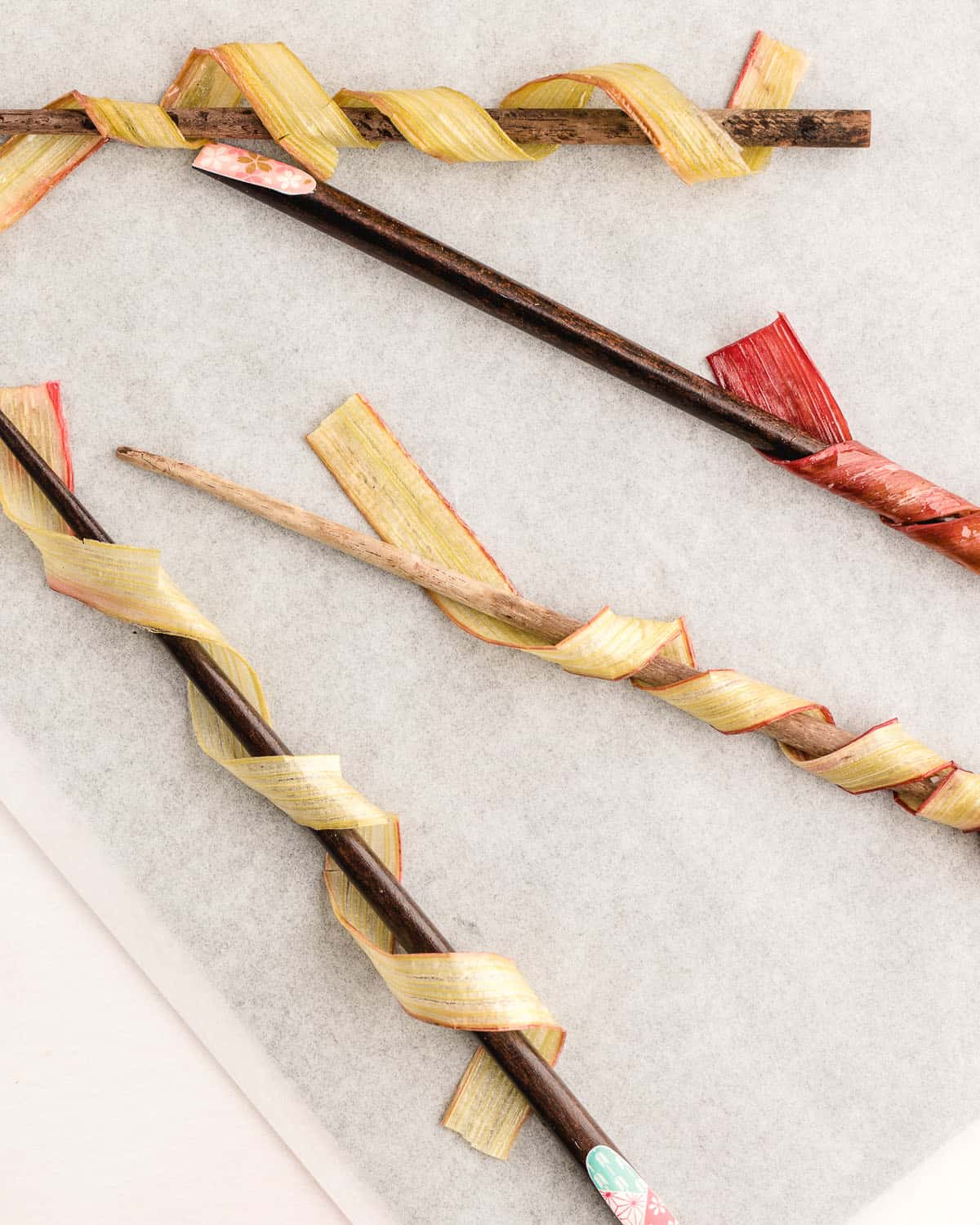 Rhubarb strips wrapped around wooden chopsticks on a parchment lined baking sheet.
