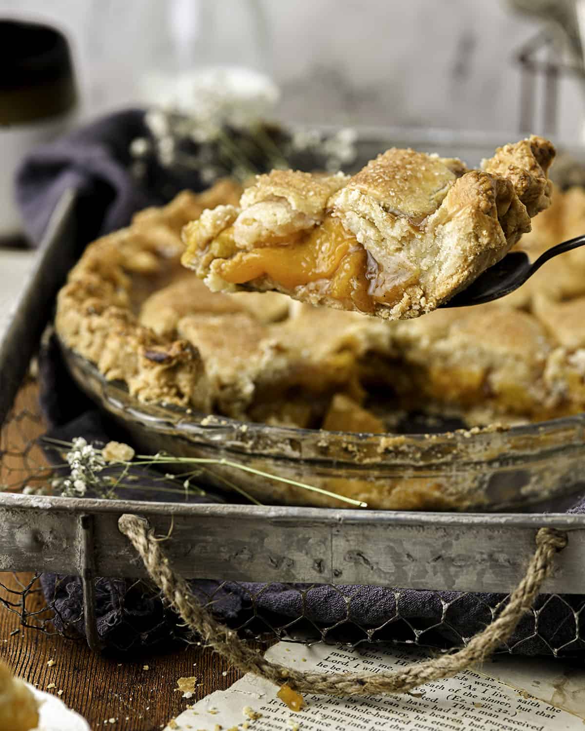 Side view of a baked fresh peach pie out of the oven on a metal pan. with a slice of pie lifted to show the delicious layers. 