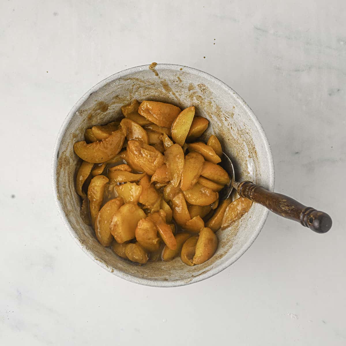 A bowl of sliced peaches being stirred with spices and sugar. 