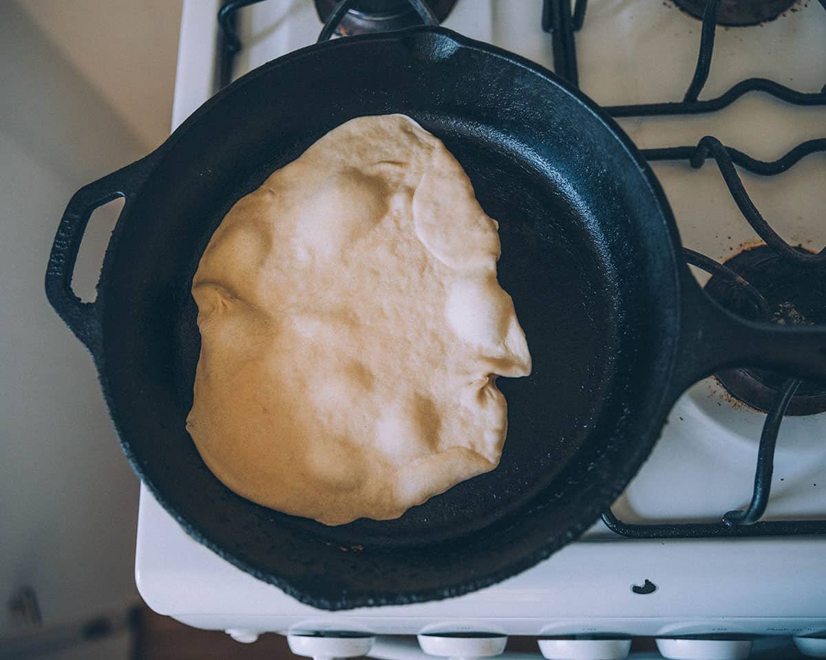 A cast iron skillet with a tortilla cooking and showing bubbles.