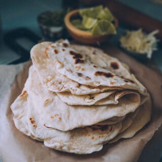 Homemade sourdough tortillas in a folded stack on a wood cutting board.