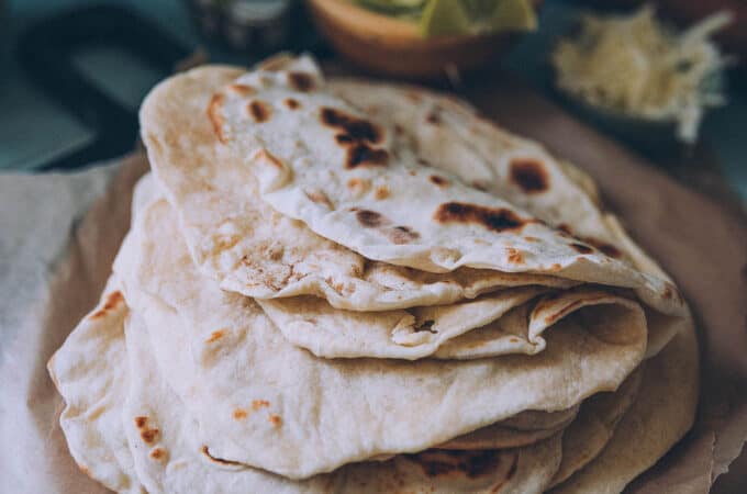 Homemade sourdough tortillas in a folded stack on a wood cutting board.