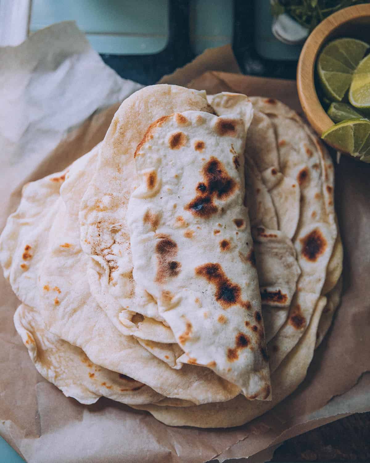 Top view of a stack of homemade sourdough tortillas, with the top few folded over showing dark cook marks. 