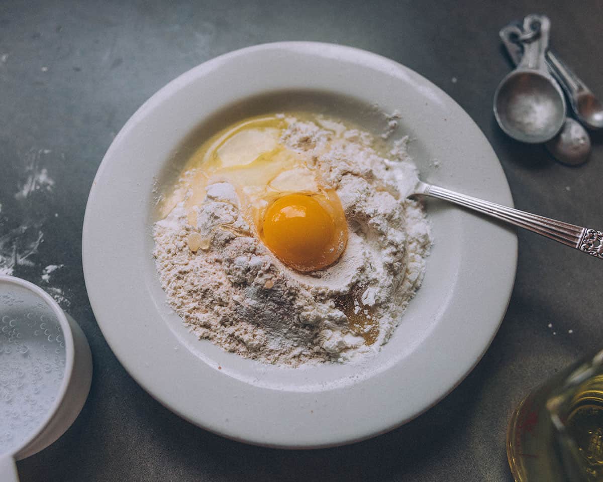 A white bowl with dry ingredients and an egg added to the top before it is stirred in. 