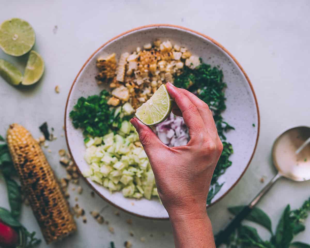 A fresh lime being squeezed into a bowl of grilled corn salad. 