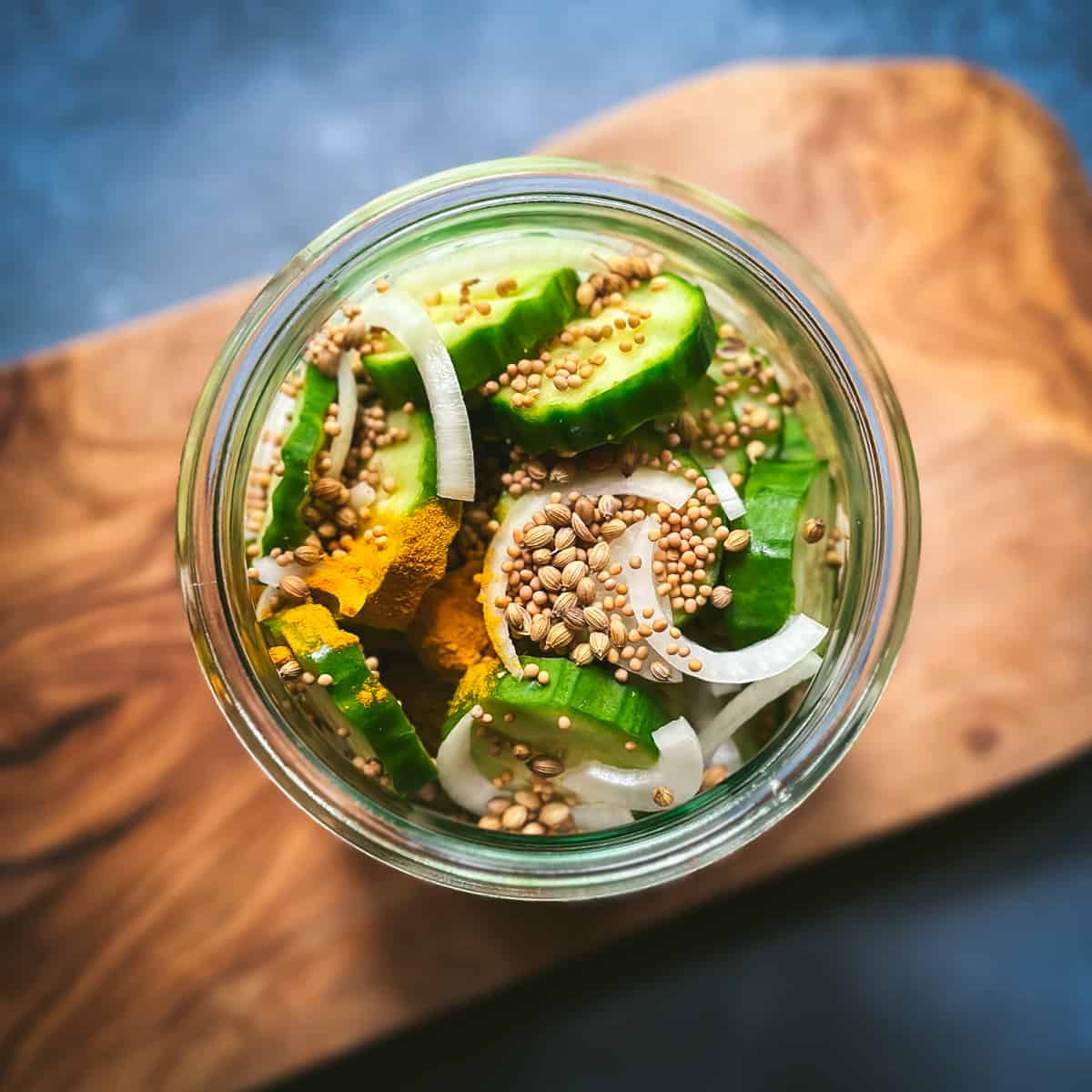 Top view of jar with sliced cucumbers, onions, and whole spices for pickling. 