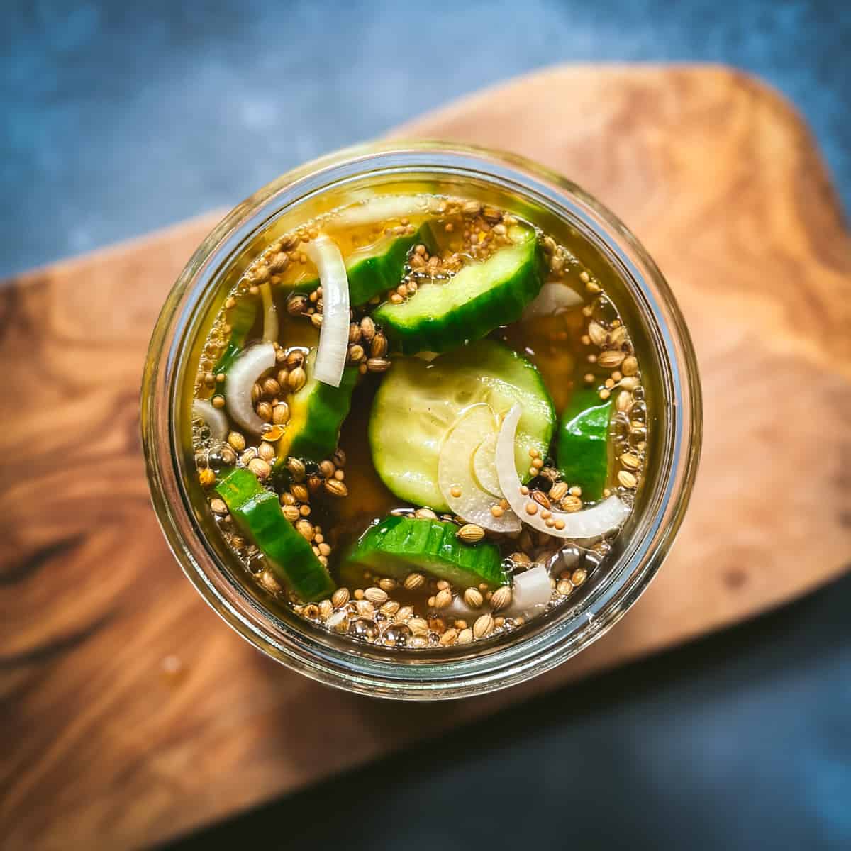 Top view of cucumbers in jar with brine on a wood cutting board.