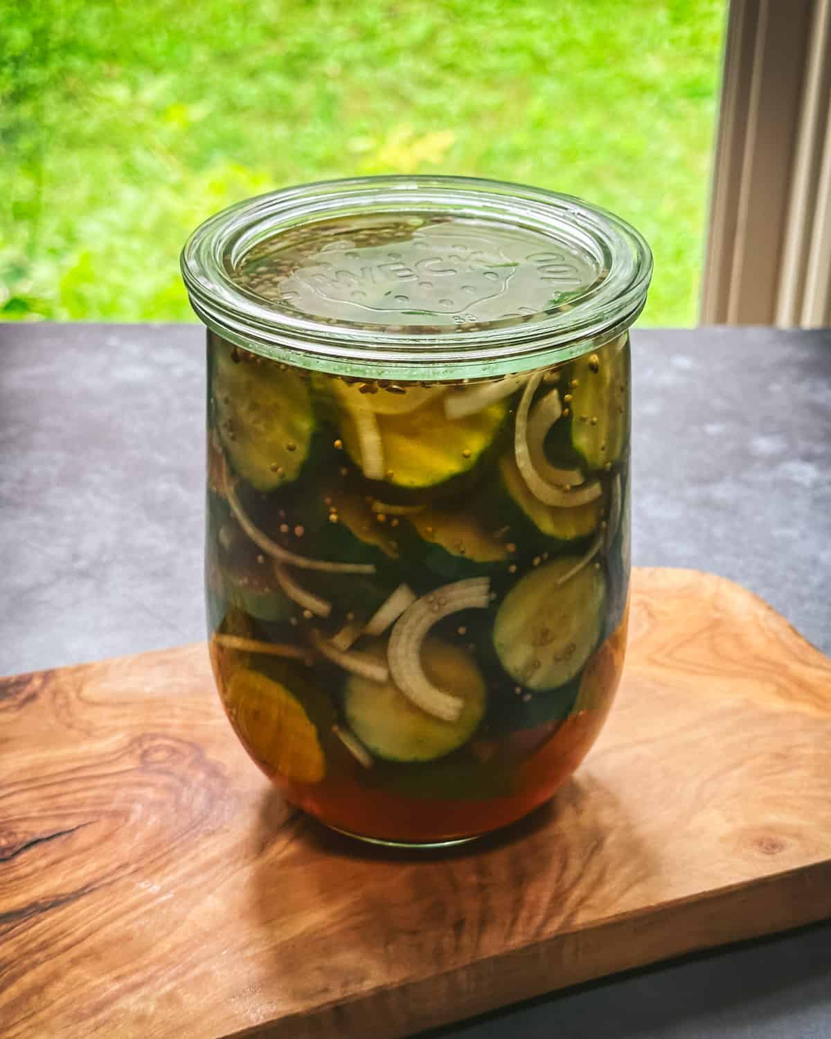Cucumbers sliced in a jar with brine with a lid on, on a wood surface. 