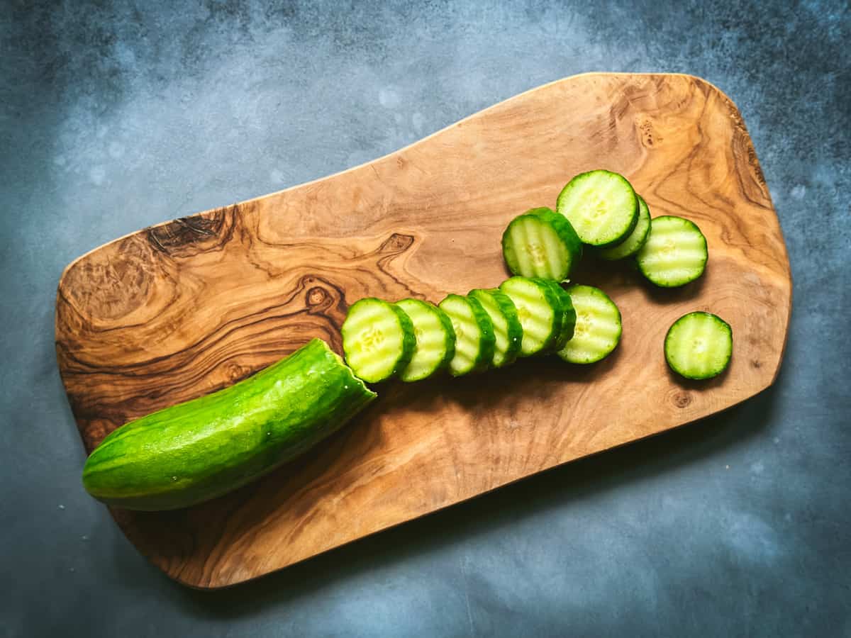 A wood cutting board with a sliced cucumber on it, gray background, top view. 